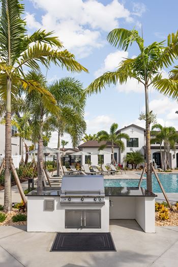 A modern outdoor kitchen with a grill and sink is surrounded by palm trees  at The Hadley - North Port, FL Apartments, North Port 34287